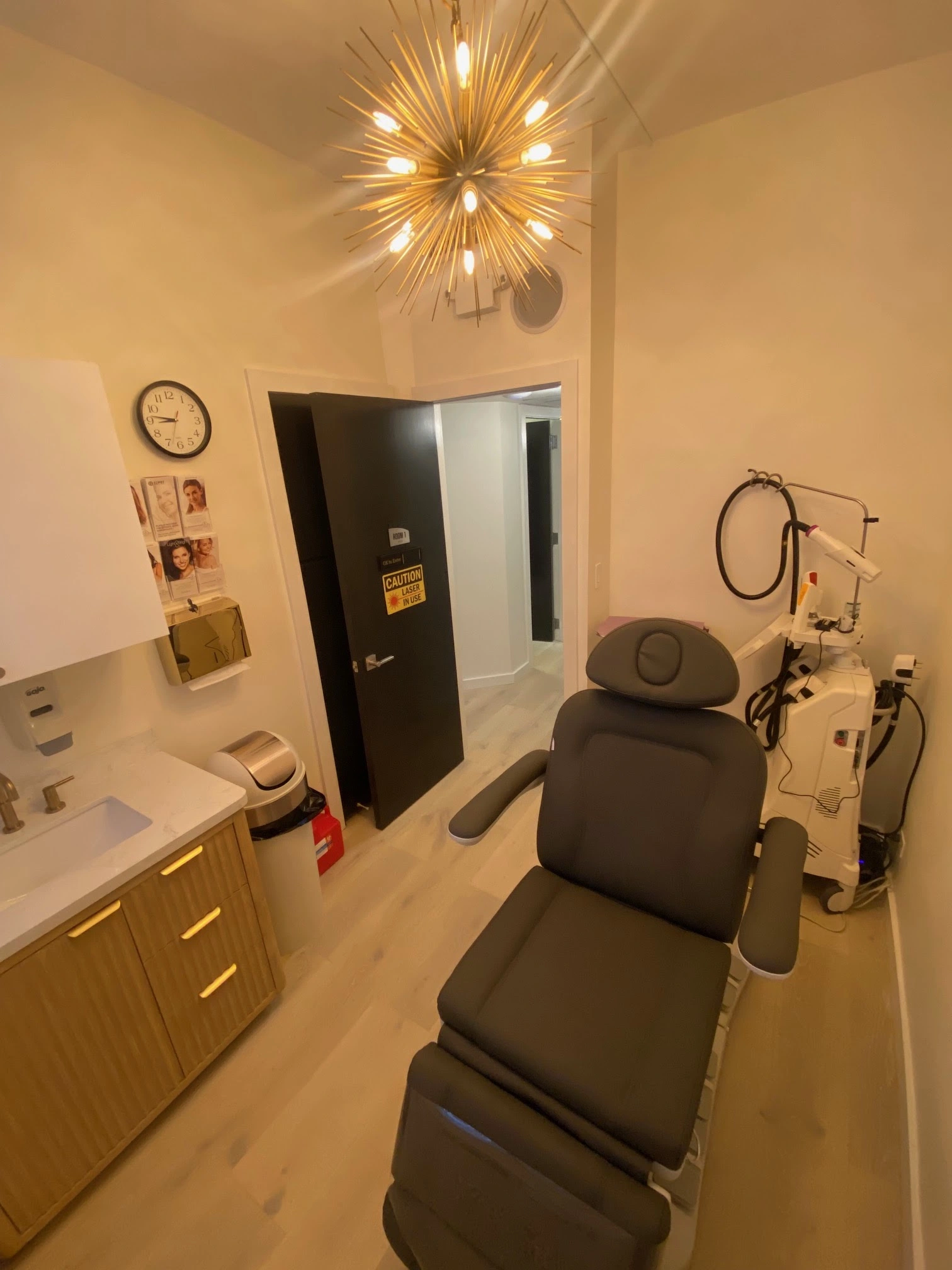 IPL treatment room at Natural Beauty Fifth Avenue with patient chair, handheld device on articulated arm, and modern fixtures